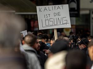 27.04.2024, Hamburg: Teilnehmer einer Islamisten-Demo halten ein Plakat mit der Aufschrift „Kalifat ist die Lösung“ in die Höhe. 