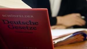 Ein Anwalt sitzt hinter der aufgeschlagenen „Schönfelder Textsammlung Deutsche Gesetze“ in einem Gericht (Symbolbild).