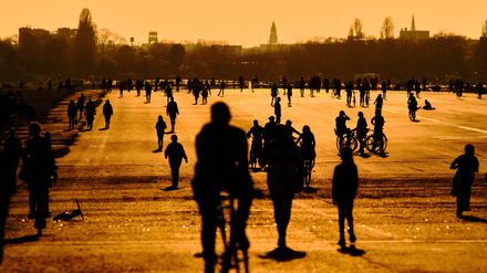 Menschen gehen im Licht der untergehenden Sonne über das Tempelhofer Feld. 