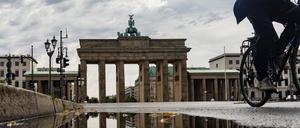 Das Brandenburger Tor spiegelt sich in einer Regenpfütze, während ein Radfahrer vorbeifährt.