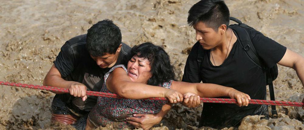 Helfer bringen eine Frau in Huachipa über eine völlig überschwemmte Straße.