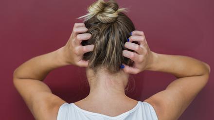 Eine Frau vor rotem Hintergrund fährt sich mit den Händen durch die Haare, um sich zu kratzen.