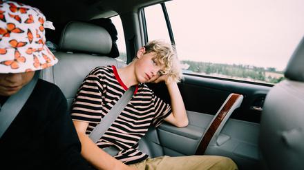 Erschöpft: Ein Junge sitzt im Auto und stützt seinen Kopf ab.