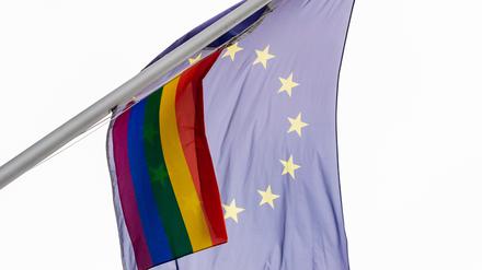 Eine Regenbogenfahne weht neben der EU-Flagge im Wind.