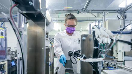 Eine junge Chemie-Laborantin mit Mundschutz und im weißen Kittel arbeitet in einem Labor an elektrochemischen Energiespeichern.