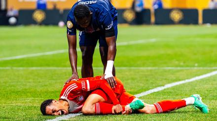 Jamal Musiala liegt mit starken Schmerzen verletzt am Boden. PSG-Profi William Pacho kümmert sich um ihn.