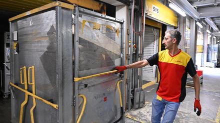 Ein Mitarbeiter bei DHL zieht einen Paketwagen.