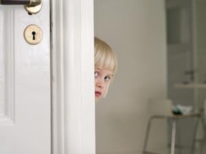 Ein scheues Kind versteckt sich hinter einer Tür.