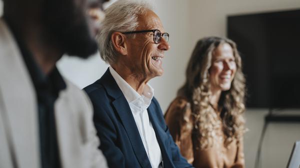 Ein älterer, fröhlicher Mann neben Kollegen im Büro