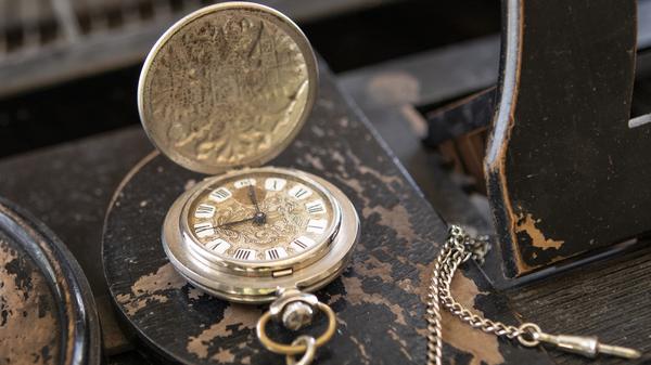Eine Vintage-Uhr liegt aufgeklappt auf einem alten Holztisch.