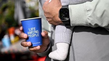 PRODUKTION - 25.09.2025, Berlin: Ein junger Mann hält einen Kaffeebecher der LAP-Kaffeekette in der Hand während er ein Baby auf dem Arm hat. (zu dpa: «Günstiger Kaffee im Trend - LAP Coffee fordert Szene heraus») Foto: Britta Pedersen/dpa +++ dpa-Bildfunk +++