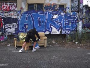 Filmstill aus Simone Zauggs Video „Home Less“: In der Rolle eines Obdachlosen lässt sich die Künstlerin von einem Graffiti-Künstler mit dem Schriftzug „Home Less“ übersprühen.