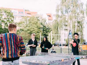 Mehrere junge Menschen spielen Tischtennis in einem Park.