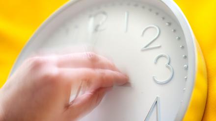 Eine Hand dreht an einer Uhr (Symbolbild).