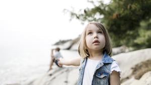 Ein etwa sechsjähriges Mädchen steht am Strand und schaut mit fragendem Blick in den Himmel.
