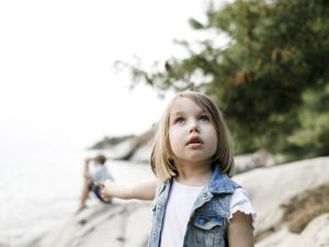 Ein etwa sechsjähriges Mädchen steht am Strand und schaut mit fragendem Blick in den Himmel.