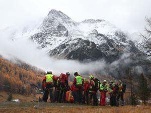 Mitglieder der Bergrettung warten vor den verschneiten Bergen des Ortler Gebirges auf den Rettungshubschrauber.