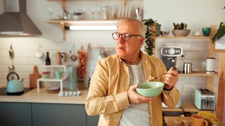 Ein älterer Mann ist im Stehen in seiner Küche ein Müsli.
