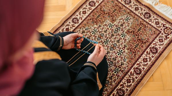 Eine Person ist von oben betend auf einem Teppich zu sehen. (Symbolbild)