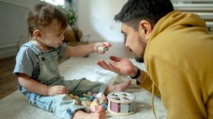 Ein Vater spielt mit seinem Sohn auf einem Teppichboden (Symbolbild)