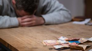 Ein Mann hat seinen Kopf auf seine Hände gelegt, während sich vor ihm Geldscheine, Münzen und Bankkarten auf einem Tisch befinden.