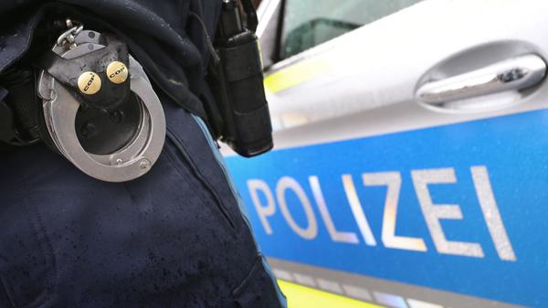 Ein Polizist mit Handschellen und einer Pistole am Gürtel steht vor einem Streifenwagen. (Symbolbild)