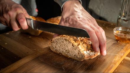 Close-up of man's hands cutting fresh loaf of bread on chopping board.
