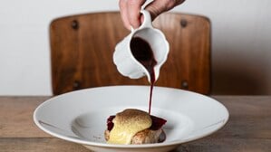 Eine Hand gieße dunkle Sauce über ein Gericht.