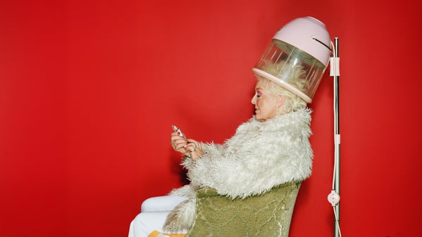 Senior woman sitting under hairdryer using mobile phone, side view