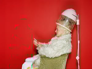 Senior woman sitting under hairdryer using mobile phone, side view