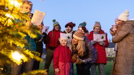 Eine Gruppe von Menschen singt draußen an einem Weihnachtsbaum Lieder.