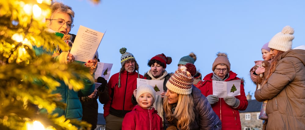 Eine Gruppe von Menschen singt draußen an einem Weihnachtsbaum Lieder.