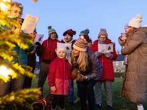 Eine Gruppe von Menschen singt draußen an einem Weihnachtsbaum Lieder.