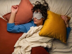 Eine schlafende junge Frau inmitten von Kissen (Symbolbild).