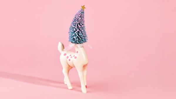 Pastel holiday scene with deer figure with Christmas tree head on pink background. Room for copy.
