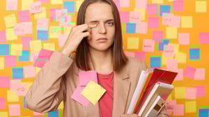 Eine Frau, beklebt mit Post-Its, reibt sich müde ihr Auge.