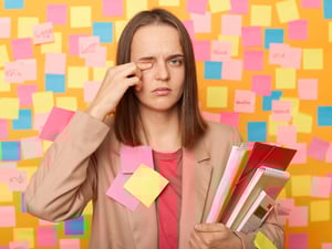 Eine Frau, beklebt mit Post-Its, reibt sich müde ihr Auge.