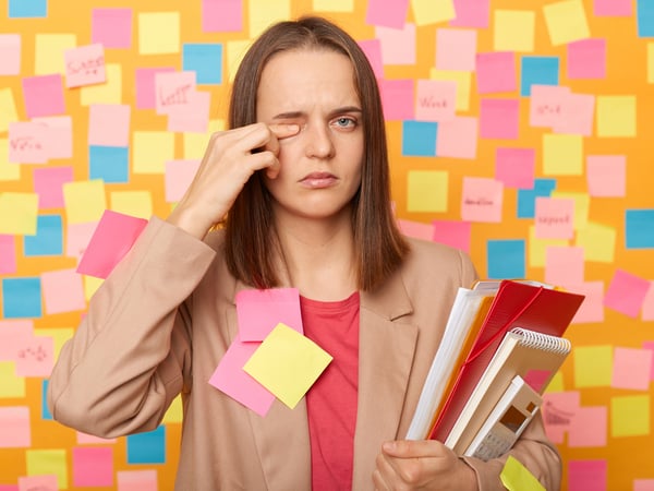 Eine Frau, beklebt mit Post-Its, reibt sich müde ihr Auge.