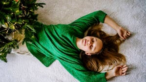 Ein Mädchen liegt mit geschlossenen Augen neben ihrem Weihnachtsbaum.