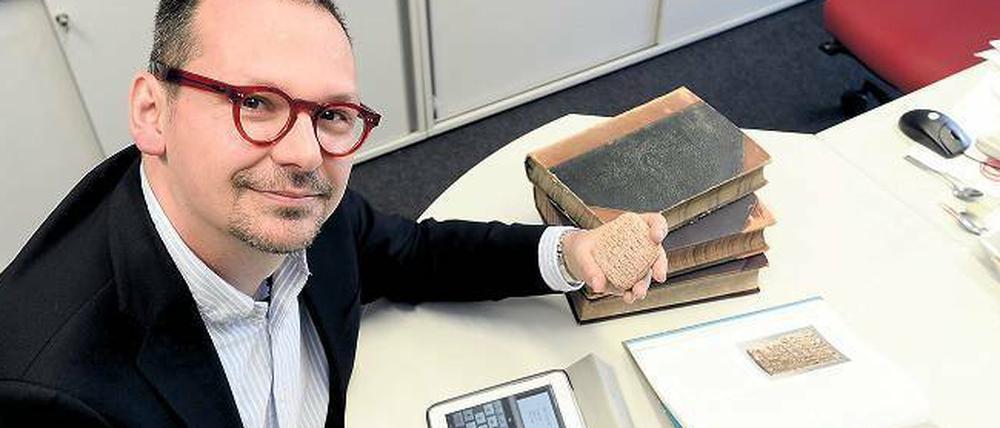 Markus Hilgert sitzt vor seinem Tablettcomputer und hält eine antike Tontafel in der Hand.