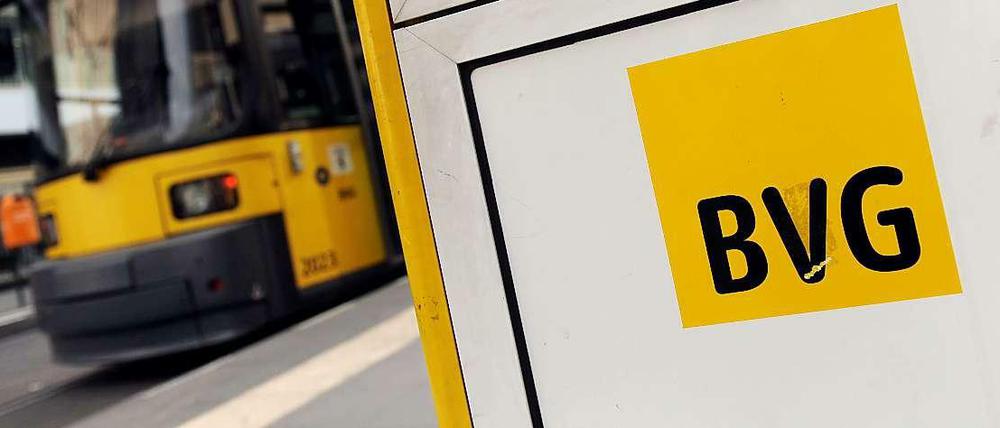 Das BVG Logo an einer Bushaltestelle mit einer Tram im Hintergrund
