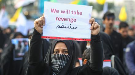 Eine Frau hält ein Schild mit der Aufschrift „Wir werden Rache ausüben“ hoch. 