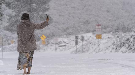 23.02.2023, USA, La Canada Flintridge: Eine Frau steht auf einer schneebedeckten Straße und macht ein Selfie im Angeles National Forest in der Nähe von La Canada Flintridge. Foto: Jae C. Hong/AP/dpa +++ dpa-Bildfunk +++