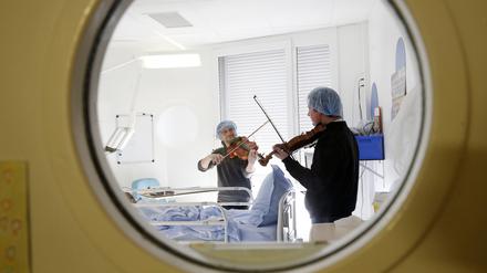 Zwei Männer spielen Geigen an einem Krankenhausbett