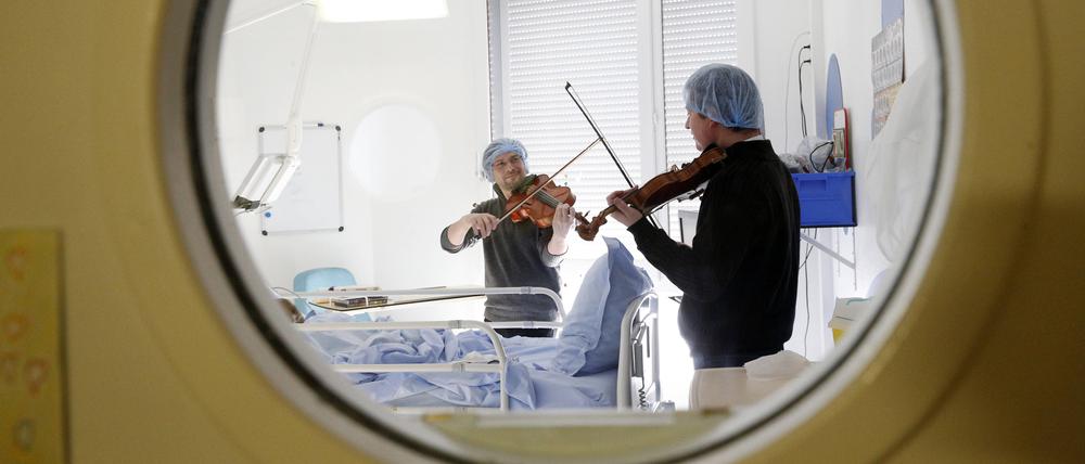 Zwei Männer spielen Geigen an einem Krankenhausbett