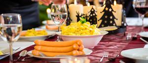 Family celebrating Christmas eve with traditional dinner Wiener sausages and potato salad, mom is filling the plates