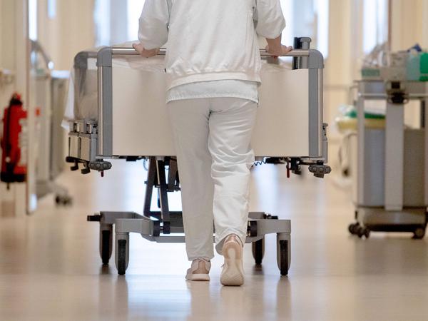 Eine Krankenpflegerin schiebt ein Krankenbett durch einen Krankenhausflur. 