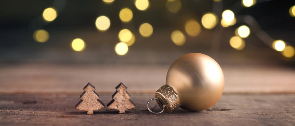 Eine goldene Weihnachtskugel und zwei kleine Holzstücke in Form von Weihnachtsbäumen.