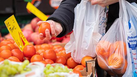 Eine Kundin begutachtet eine Tomate an einem Stand auf einem Wochenmarkt.