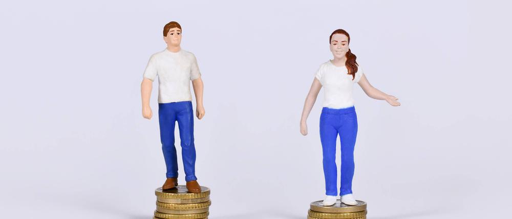 Konzept des geschlechtsspezifischen Lohngefälles mit einem Mann und einer Frau, die auf einer unterschiedlichen Anzahl von Münzen stehen